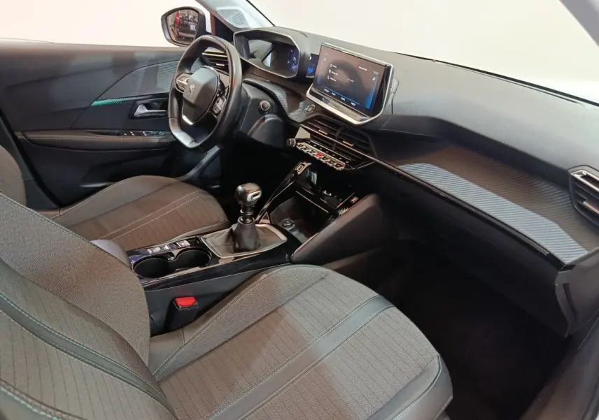 Vue intérieure côté conducteur de la Peugeot 208 blanche, montrant le tableau de bord et la console centrale avec écran tactile.