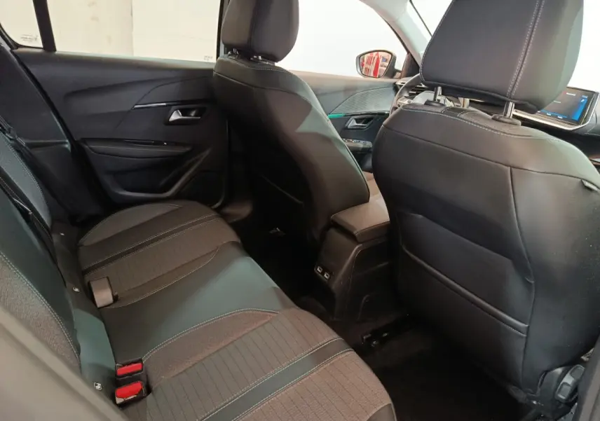 Vue intérieure arrière côté gauche de la Peugeot 208 blanche, montrant la banquette et les sièges avant en cuir noir.