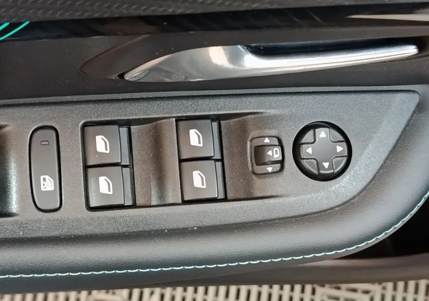 Gros plan sur les commandes de lève-vitres et réglages des rétroviseurs côté conducteur d’une Peugeot 208 blanche.