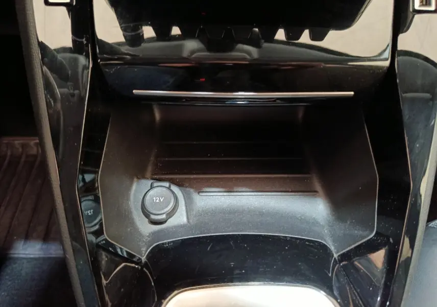 Gros plan sur la prise 12V et le rangement central noir brillant de la Peugeot 208 blanche, intérieur avant.