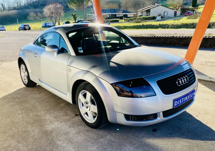 Audi TT Coupé gris vue 3/4 avant droit, avec jantes alliage et calandre noire sous un abri orange.