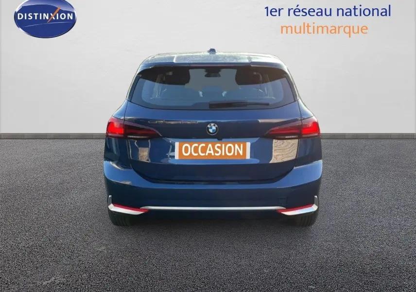 Vue arrière d'une BMW Série 2 Active Tourer 218i bleu phytonique métallisé avec feux arrière allumés sur fond neutre.