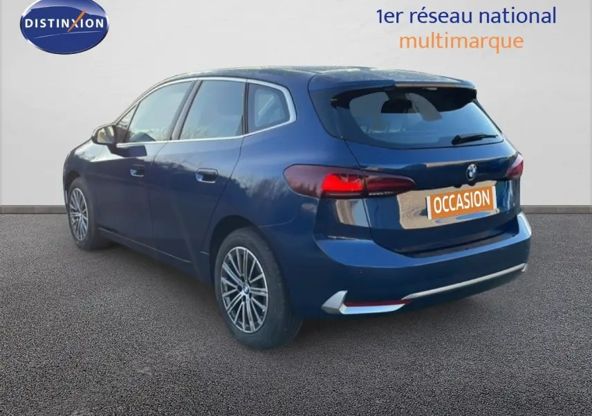 BMW Série 2 Active Tourer 218i bleu phytonique métal vue 3/4 arrière droit avec feux arrière allumés.