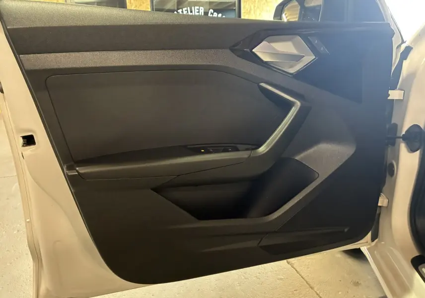 Vue intérieure de la porte avant gauche blanche d'une Audi A1 2022, avec garniture noire et poignée argentée.