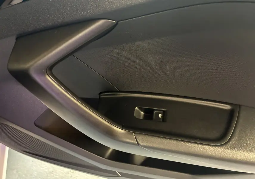 Gros plan sur la poignée intérieure noire de la porte côté gauche d'une Audi A1 blanche, avec bouton de commande de vitre.