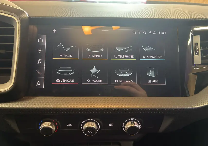 Vue rapprochée de l'écran tactile central et des commandes de climatisation dans l'habitacle d'une Audi A1 blanche 2022.