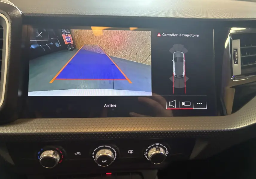 Écran central de l'Audi A1 blanc montrant la caméra de recul avec aide au stationnement et contrôle de trajectoire.