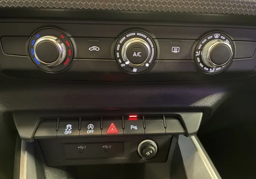 Gros plan sur les commandes de climatisation et les boutons de fonction d'une Audi A1 blanche, intérieur noir.