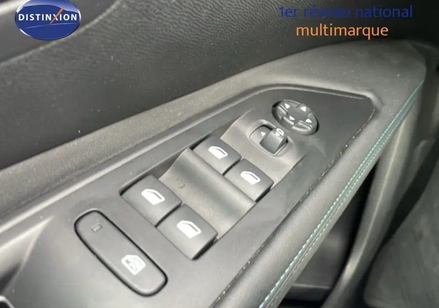 Gros plan sur les commandes des vitres et rétroviseurs côté conducteur, avec surpiqûres bleues sur la garniture noire.