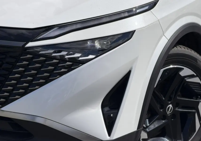 Gros plan sur l'avant droit du Nissan Qashqai blanc nacré avec calandre noire et jante alliage 18 pouces.