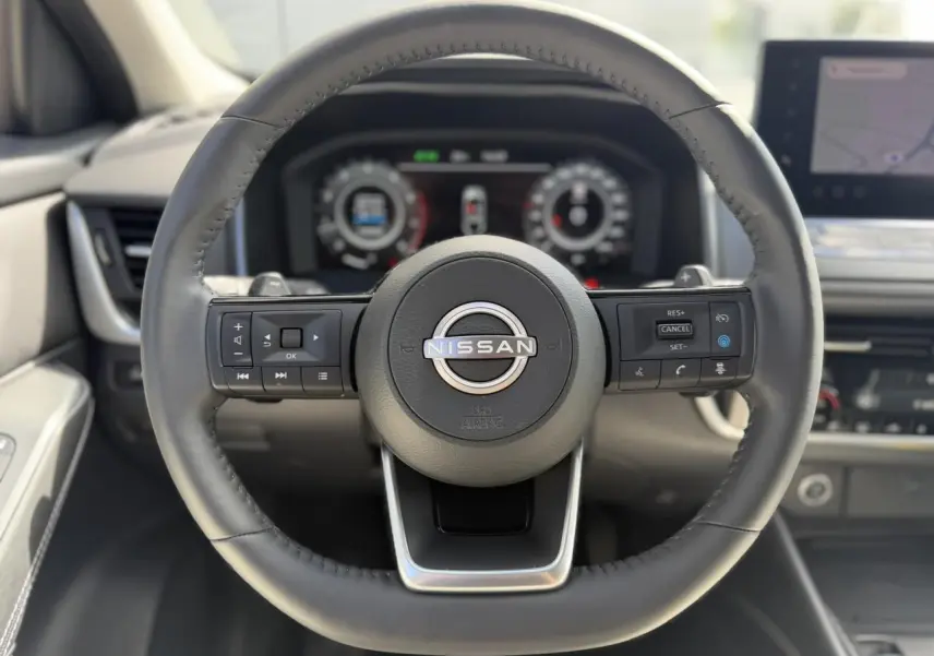 Vue rapprochée du volant cuir noir du Nissan Qashqai 2025 avec commandes intégrées et tableau de bord numérique flou.