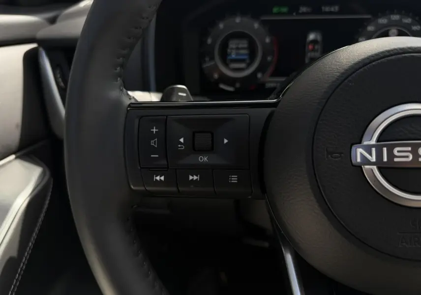 Gros plan sur le volant cuir noir du Nissan Qashqai 2025 avec commandes audio et affichage numérique en arrière-plan flou.