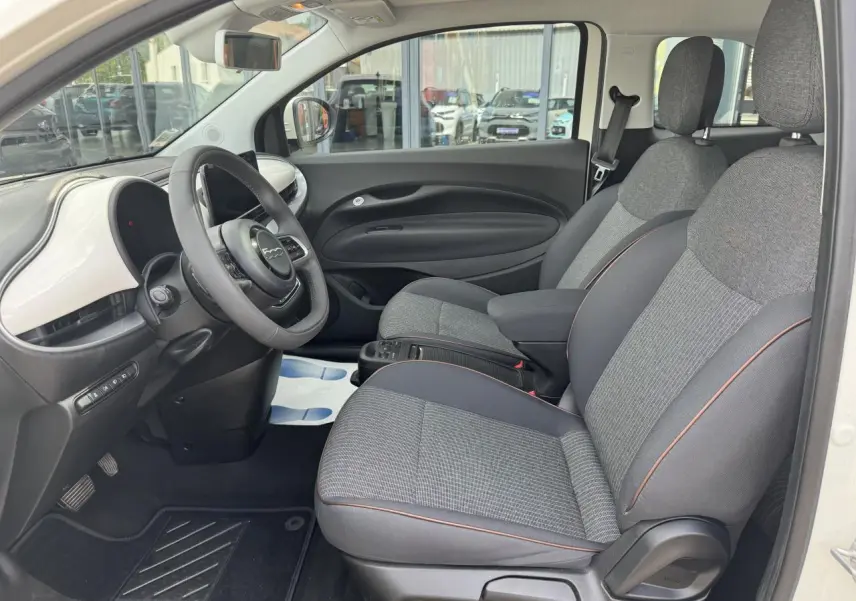 Vue intérieure côté conducteur de la Fiat 500 électrique blanche 2022 avec sellerie gris anthracite et planche de bord blanche.