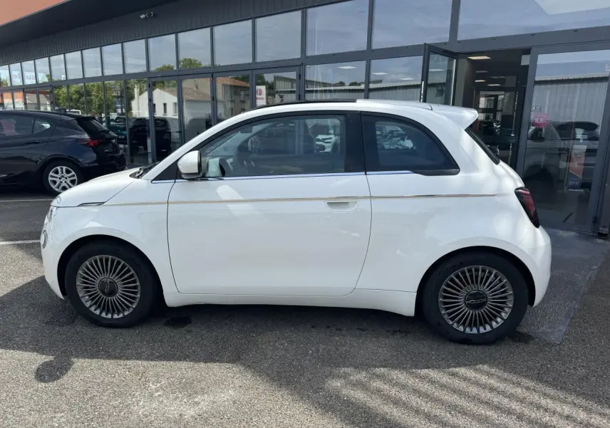 Profil côté gauche d'une Fiat 500 électrique blanche 2022 avec jantes alliage 16 pouces et toit panoramique.