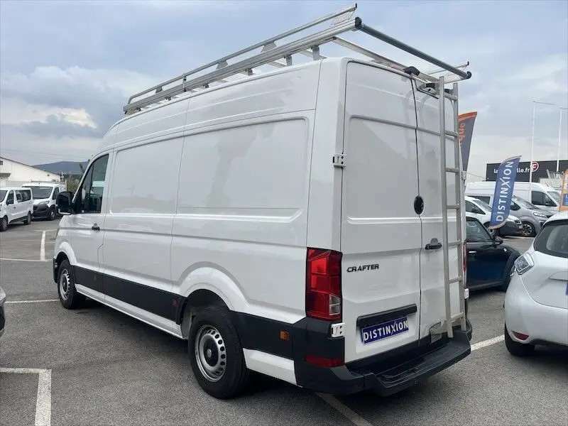 Vue 3/4 arrière droite d'un Volkswagen Crafter blanc avec galerie et échelle métallique sur le toit, stationné en extérieur.