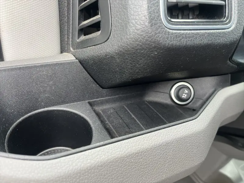 Prise 12V et porte-gobelet noirs dans l'habitacle du Volkswagen Crafter Fourgon blanc, vue rapprochée côté passager.