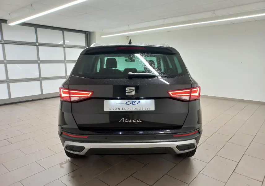 Vue arrière d'un SEAT Ateca noir Magic Nacré avec feux allumés et hayon électrique dans un garage lumineux.