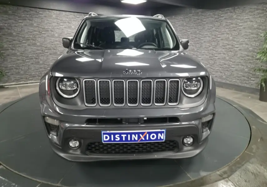 Vue avant d'un Jeep Renegade gris métallisé avec calandre noire et feux LED ronds dans un showroom.