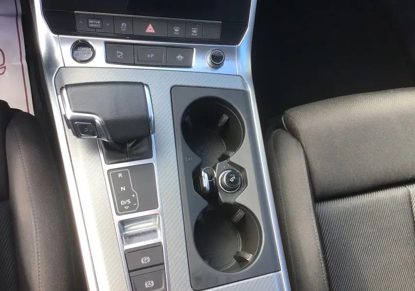 Vue rapprochée de la console centrale de l’Audi A6 Avant blanc glacier 2022, avec levier de vitesse automatique et porte-gobelets.