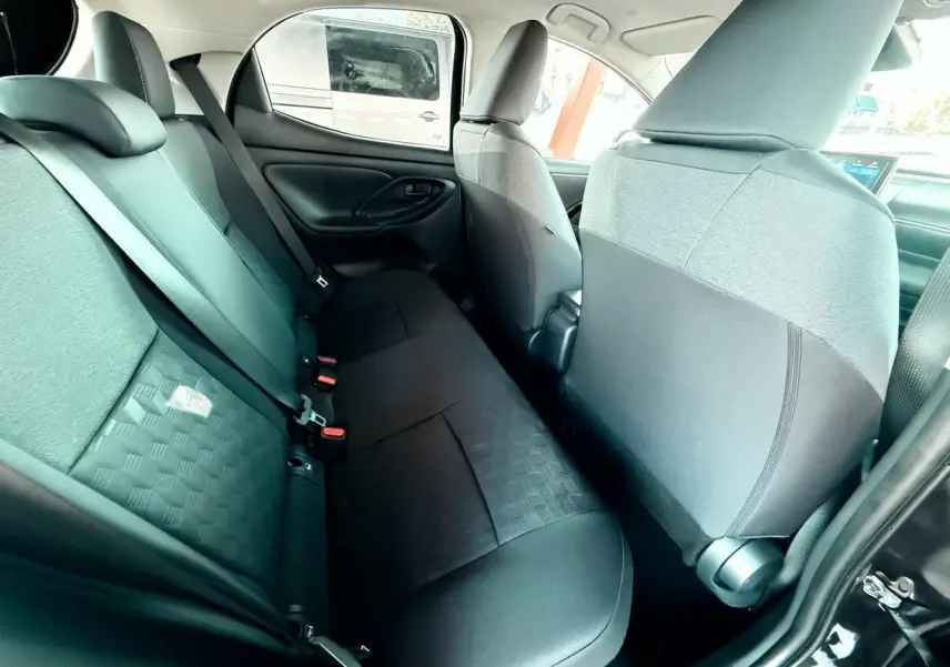 Intérieur arrière de la Toyota Yaris Hybrid 2025, sièges noirs en tissu avec motifs géométriques, vue côté gauche.