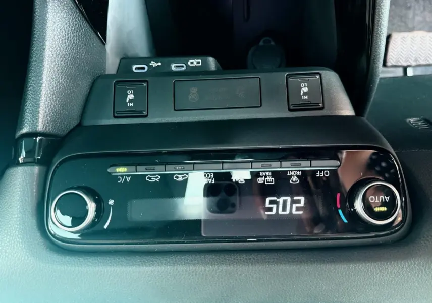 Vue rapprochée de la console centrale noire de la Toyota Yaris Hybrid 2025 avec commandes climatisation et ports USB.