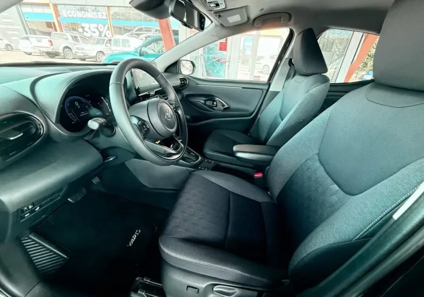 Intérieur côté conducteur de la Toyota Yaris Hybrid 2025, sièges noirs et tableau de bord moderne avec écran tactile.