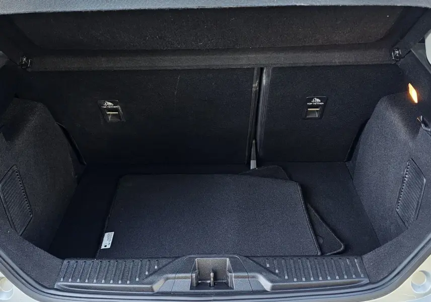Coffre ouvert d'une Ford Fiesta gris lunaire métal 2021, montrant l'espace de rangement et les tapis noirs à l'intérieur.