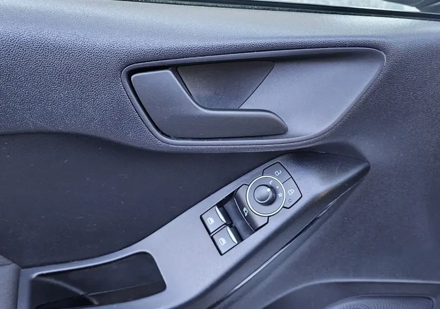 Gros plan sur la porte côté gauche d'une Ford Fiesta gris lunaire, montrant la poignée et les commandes des vitres et rétroviseurs.