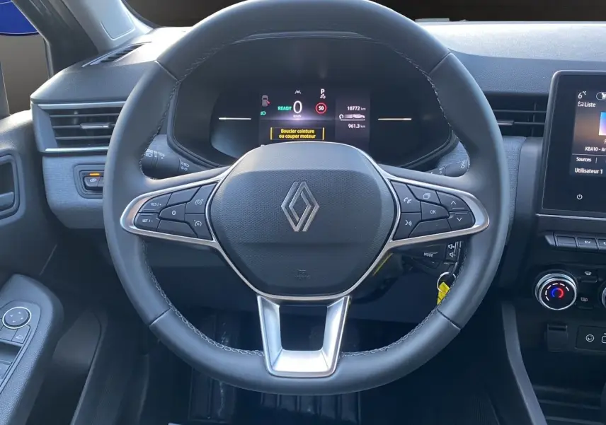 Vue rapprochée du volant noir de la Renault Clio V E-Tech avec tableau de bord numérique et commandes intégrées.