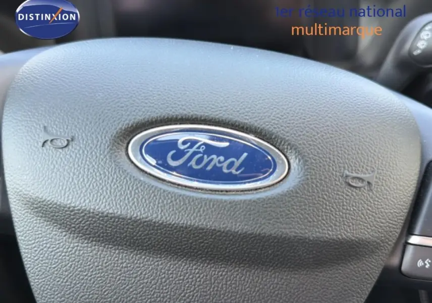 Gros plan sur le volant noir avec logo Ford au centre, intérieur du Ford Kuga 2024 visible en arrière-plan.