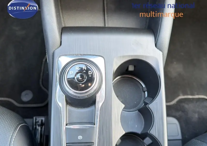 Vue plongeante sur la console centrale noire du Ford Kuga 2024 avec sélecteur rotatif de boîte auto et porte-gobelets.