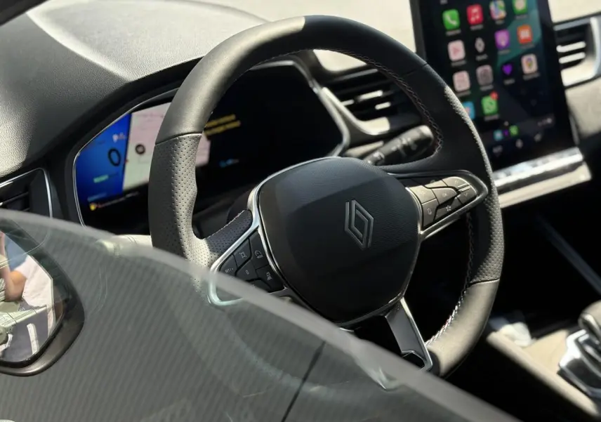 Vue rapprochée du volant noir avec logo Renault sur le tableau de bord numérique et écran tactile du Renault Symbioz.