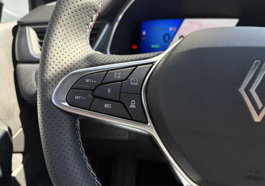 Gros plan sur le volant perforé avec surpiqûres bleu blanc rouge du Renault Symbioz 2025, boutons de commande visibles.