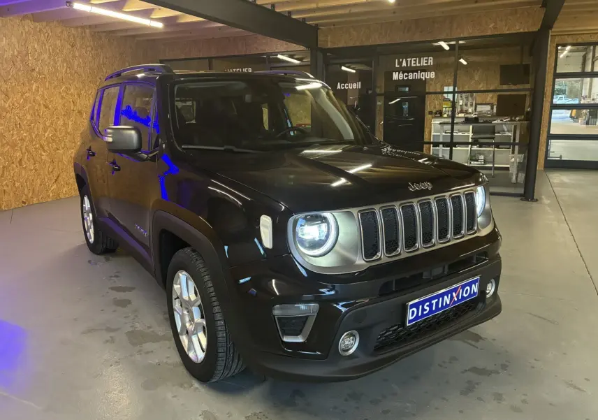 Jeep Renegade noir vue 3/4 avant droit dans un garage avec phares allumés et calandre distinctive chromée.
