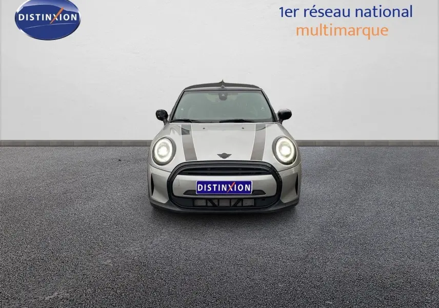 Vue frontale d'une MINI Cabriolet 2023 couleur Melting Silver Metal avec phares allumés et bandes noires sur le capot.