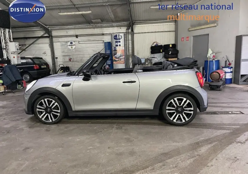 Profil droit d'une MINI Cabriolet 2023 couleur Melting Silver Metal avec capote ouverte dans un garage.