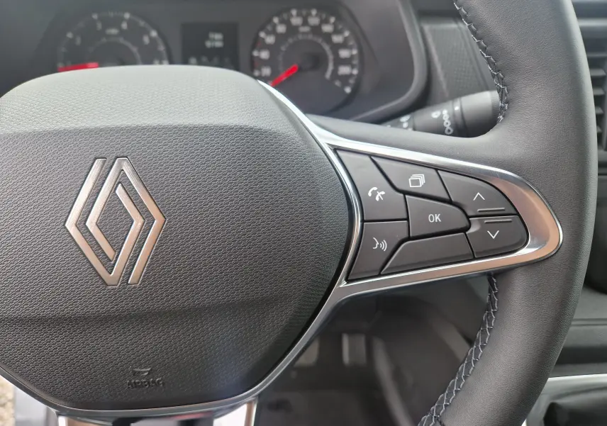 Gros plan sur le volant côté droit du Renault Trafic Fourgon gris urbain 2025 avec commandes intégrées et tableau de bord flou.