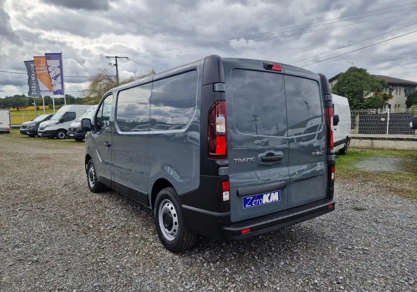 Vue 3/4 arrière droite d'un Renault Trafic Fourgon gris urbain 2025, avec feux arrière et porte arrière visibles.