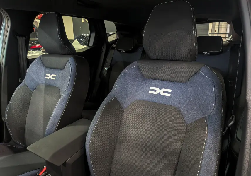 Gros plan sur les sièges avant en tissu bleu et noir du Dacia Duster 2025, avec logo distinctif brodé.