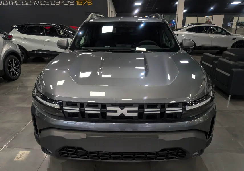 Vue de face du Dacia Duster 2025 gris schiste avec sa calandre distinctive et ses phares fins en showroom.