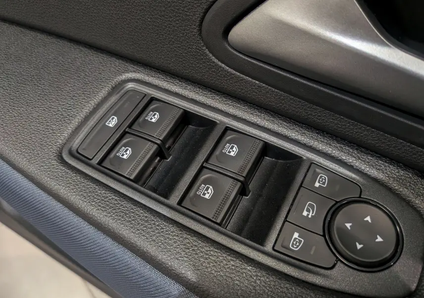 Gros plan sur les commandes électriques des vitres et rétroviseurs côté conducteur du Dacia Duster gris Schiste 2025.