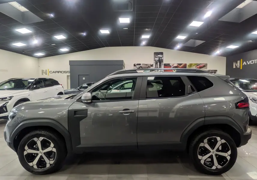 Profil côté gauche du Dacia Duster gris schiste 2025 en version Mild Hybrid 130 CH 4x4 JOURNEY, en showroom lumineux.