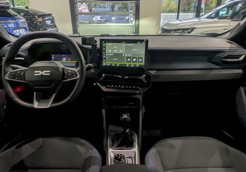 Vue intérieure du tableau de bord du Dacia Duster 2025, avec volant multifonction et écran tactile central.