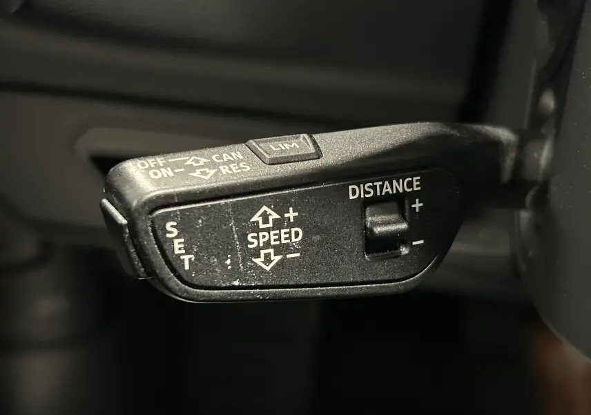 Gros plan sur la commande de régulateur de vitesse de l'Audi A6 Avant 40 TDI noire, avec réglage de la distance et vitesse.