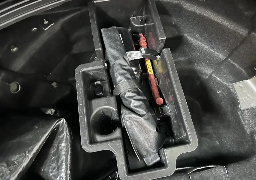 Rangement sous le coffre de l'Audi A6 Avant noir 2019 montrant un kit de secours et outils organisés.