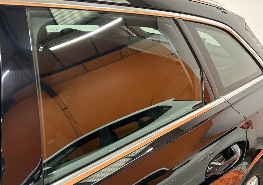 Gros plan sur la porte arrière droite noire d'une Audi A6 Avant 40 TDI 2019, reflet et intérieur cuir marron visibles.