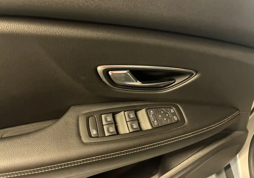 Gros plan sur la poignée de porte intérieure noire et les commandes des vitres du côté gauche du Renault Grand Scenic gris 2017.