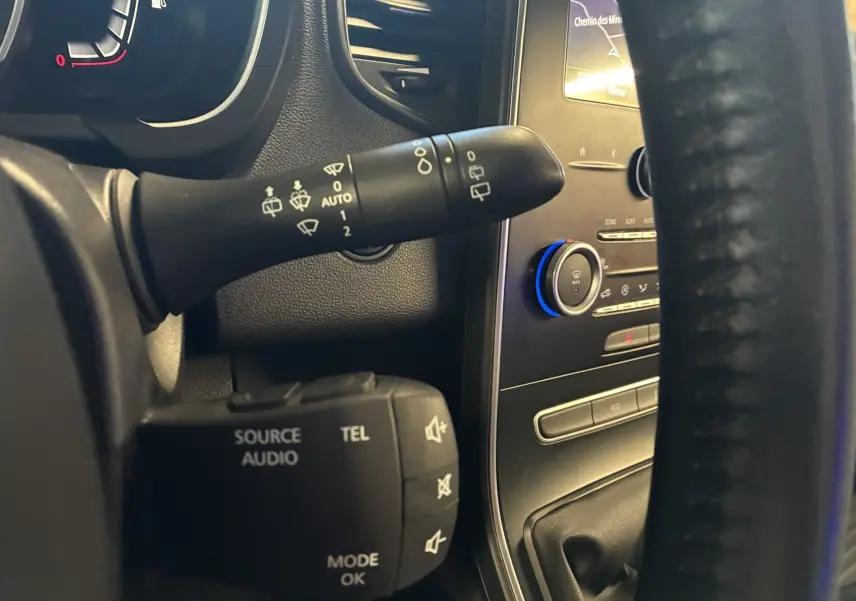 Gros plan intérieur sur les commandes au volant d'un Renault Grand Scenic gris, mettant en valeur les commandes audio et essuie-glace.