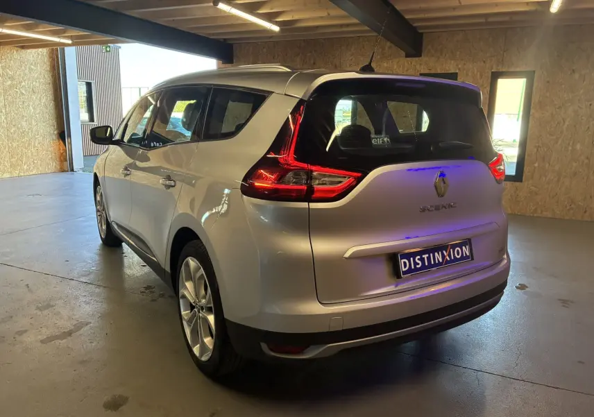 Vue 3/4 arrière droite d'un Renault Grand Scenic gris 2017 avec feux arrière LED et toit panoramique en intérieur.