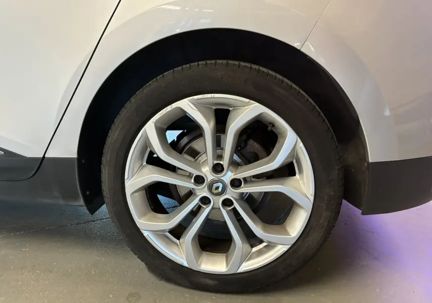 Gros plan sur la roue arrière droite d'un Renault Grand Scenic gris, avec partie de la carrosserie visible.